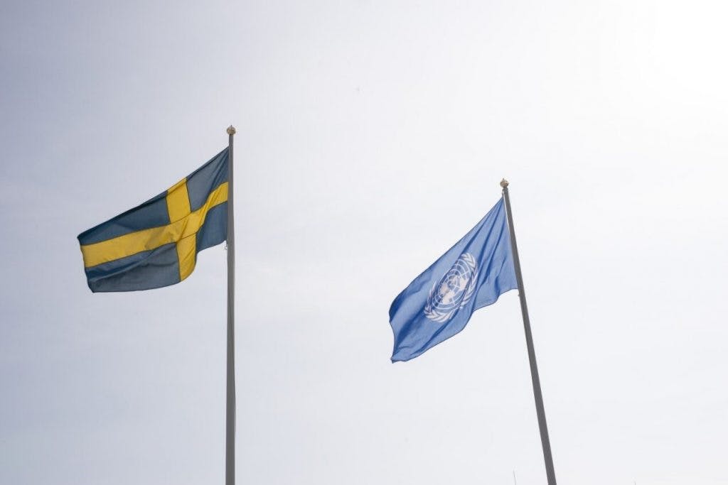 Den svenska flaggan och FN:s flagga vajar mot en blågrå himmel